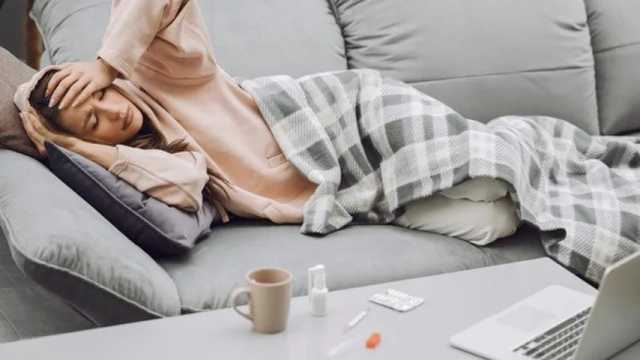 Mujer enferma con malestar general y dolor de cabeza, tumbada en el sofá de casa. (Foto: Freepik)