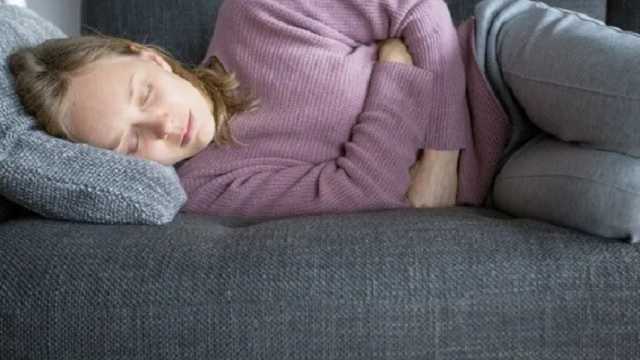 Mujer joven acostada en un sofá con molestias estomacales. (Foto: Freepik)