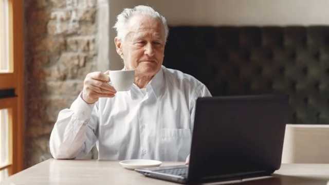 Hombre mayor tomando café mientras lee en su ordenador portátil. (Foto: Amazon)